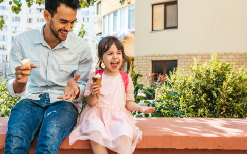 Image of happy cute little girl sitting with dad on the city street and eating ice-cream outdoor. Fun girl kid and father have fun and playing outside. Good relationship between dad and daughter