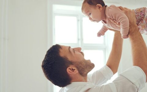 Smiling young father standing at home playfully holding his adorable baby girl up in the air